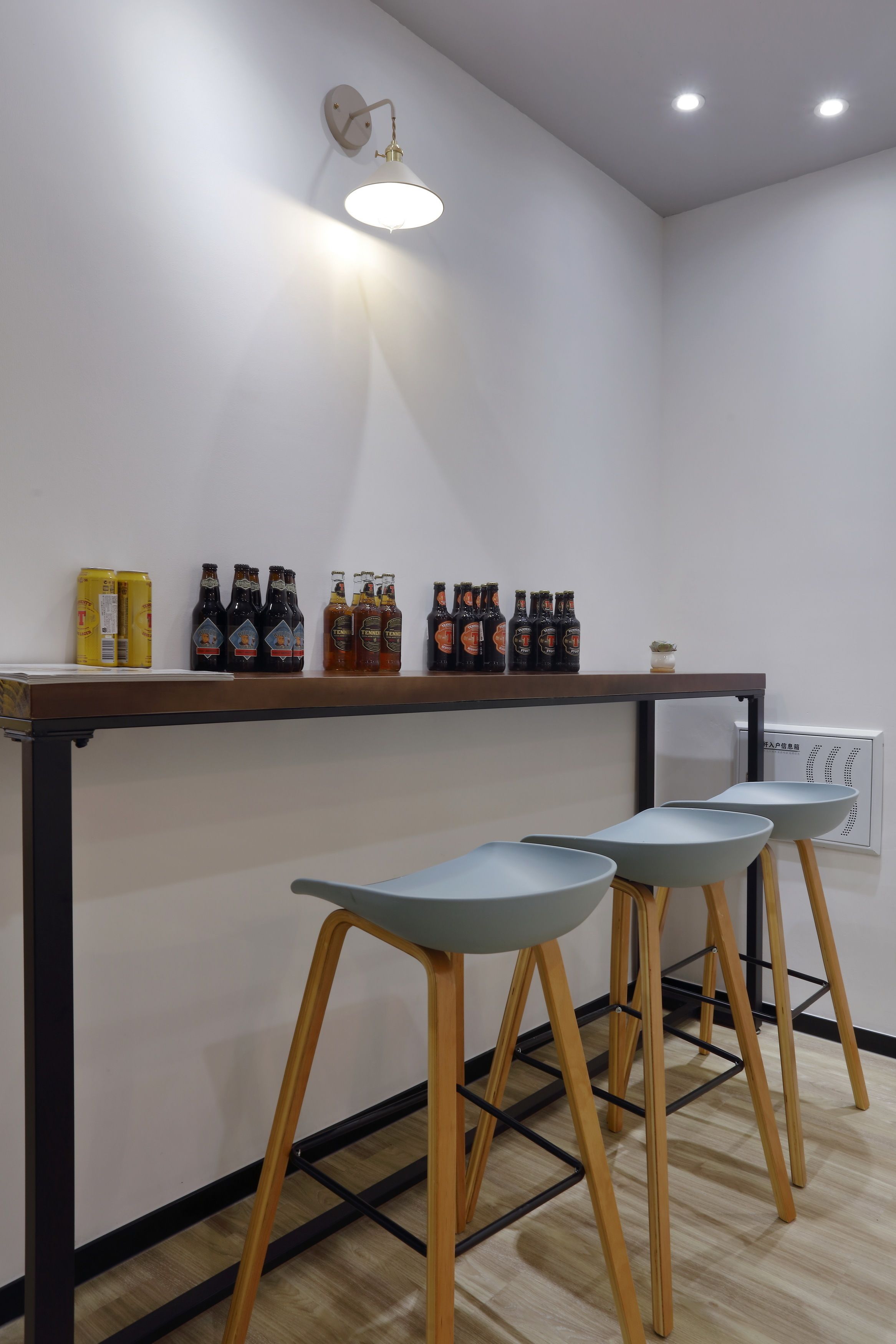 A modern kitchen with a bar area, featuring a wooden bar counter, stools, and a wall-mounted light fixture.