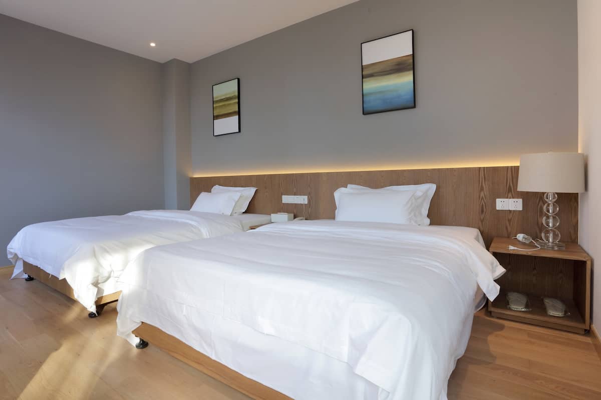 Une chambre d’hôtel avec deux lits, des têtes de lit en bois, des tables de chevet et des œuvres d’art accrochées au mur.