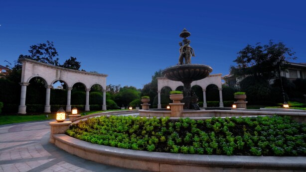A fountain with a statue in the center, surrounded by a circular garden and a pathway. - The Moment We Met (Changzhou)