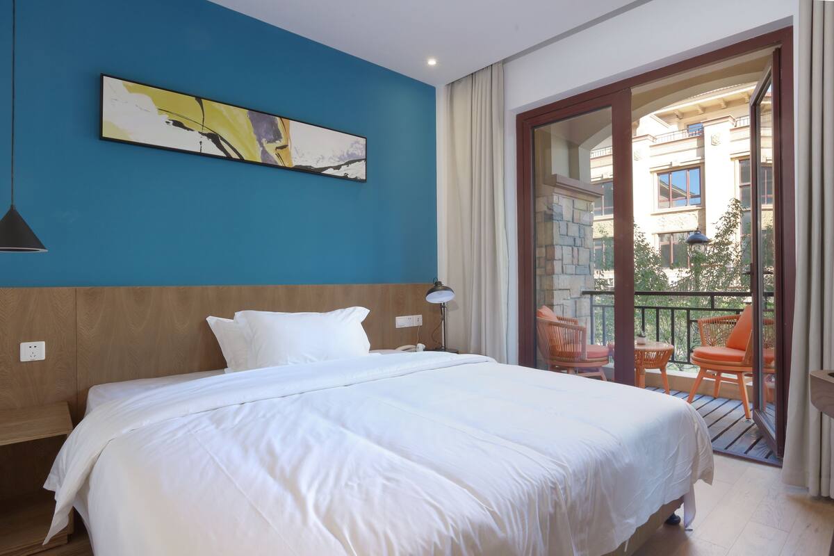Une chambre d’hôtel avec un grand lit, un tableau au mur et un balcon avec des meubles d’extérieur.