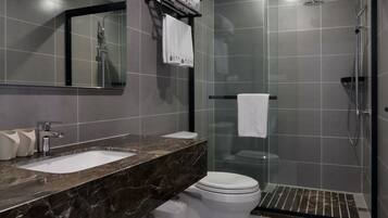 A modern bathroom with a marble sink, a toilet, a glass-enclosed shower, and a large mirror.