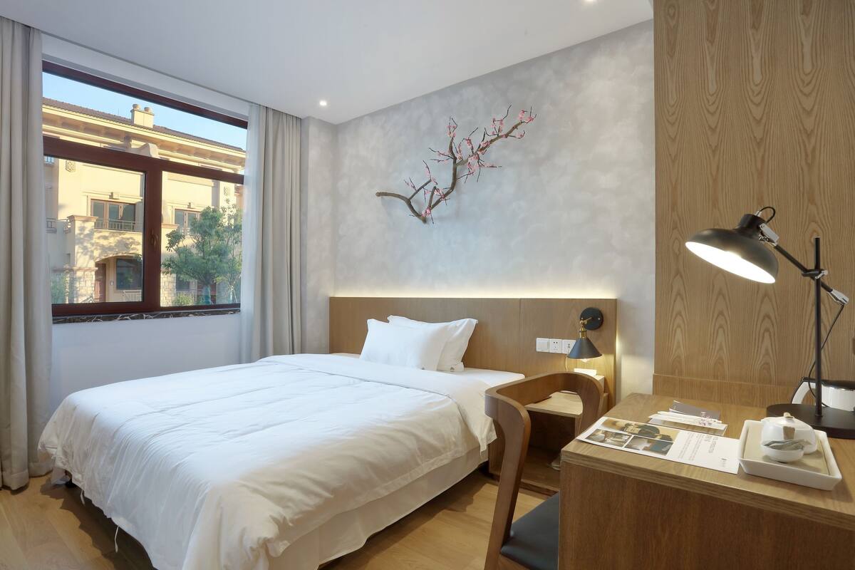 Une chambre d’hôtel avec un lit, un bureau doté d’une lampe, un mur en bois et une fenêtre avec des rideaux.