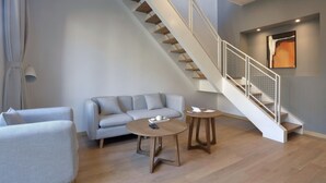 A modern living room with a grey sofa, two round wooden tables, and a staircase with a white railing. - The Moment We Met (Changzhou)