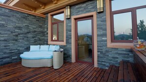 A modern outdoor seating area with a stone wall, a cushioned bench, and a glass door leading to a deck. - The Moment We Met (Changzhou)