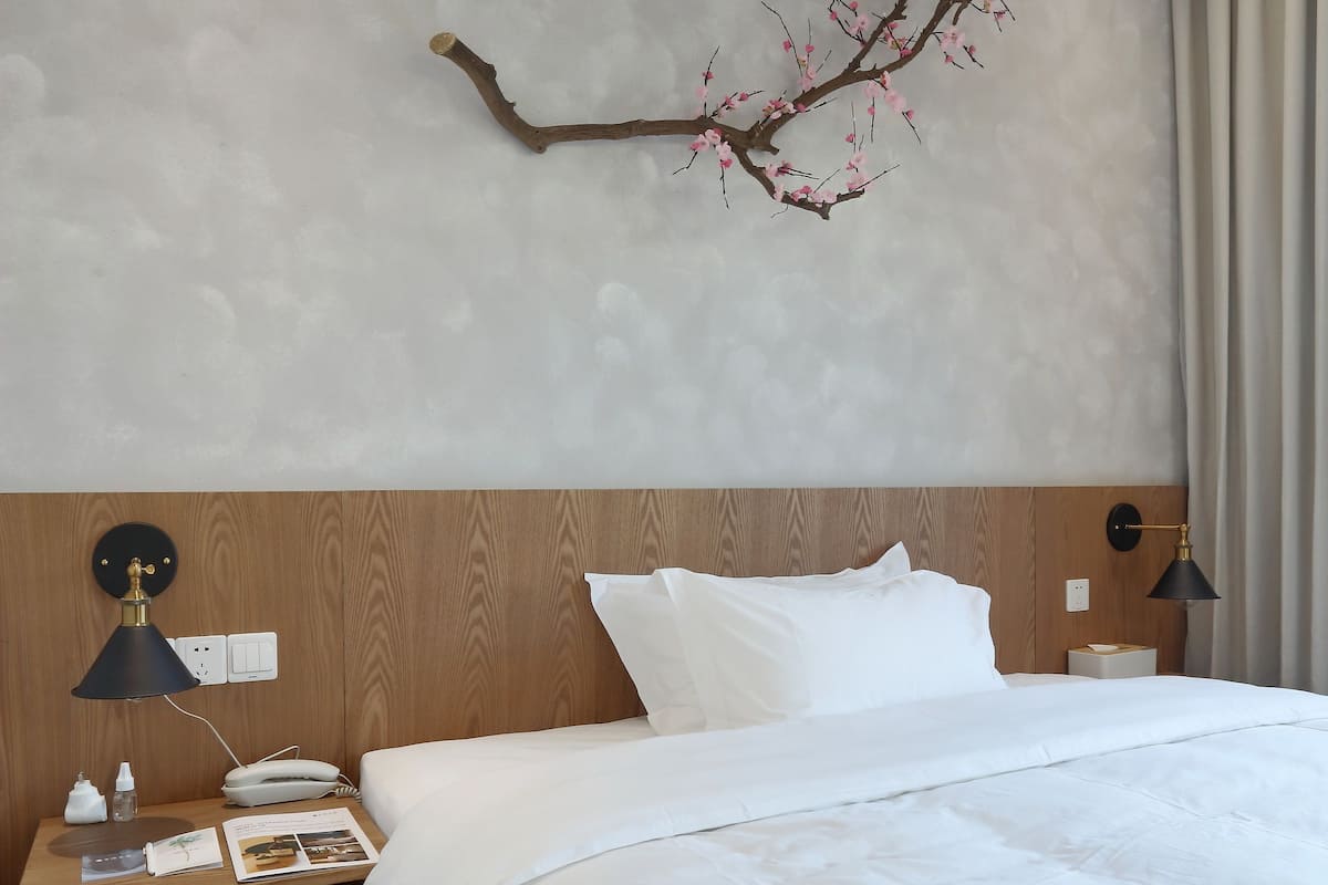 Une chambre d’hôtel comprenant un lit, des tables de chevet, une lampe, une décoration murale en forme de branche et une tête de lit en bois.