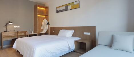 A modern hotel room with a large bed, a desk, a chair, and a bedside table.