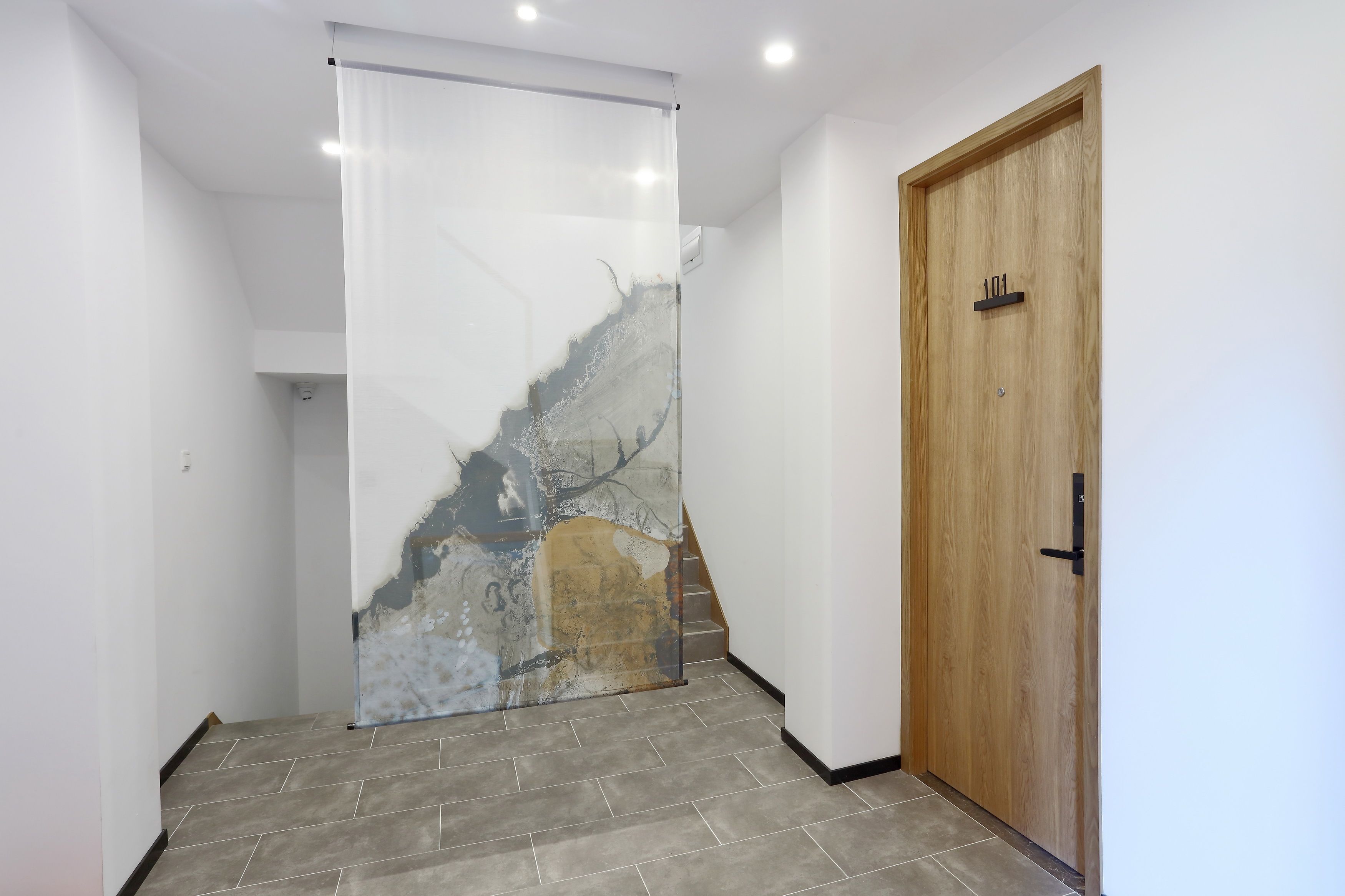 Un pasillo con puerta de madera, separador de vidrio con diseño tipo piedra y suelo de baldosas grises.