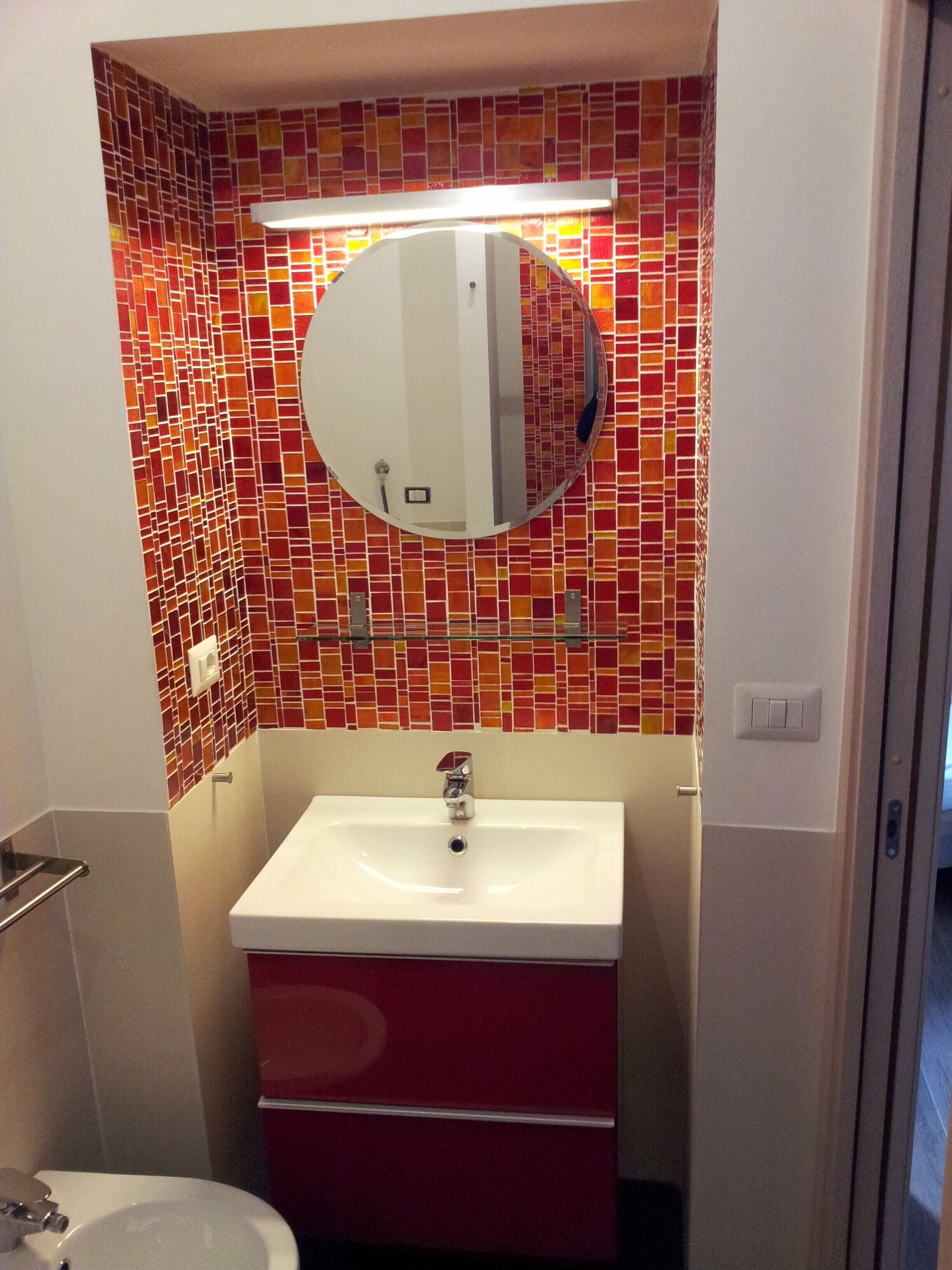 Een badkamer met een witte wastafel, een rode kast en een betegelde muur met mozaïek.