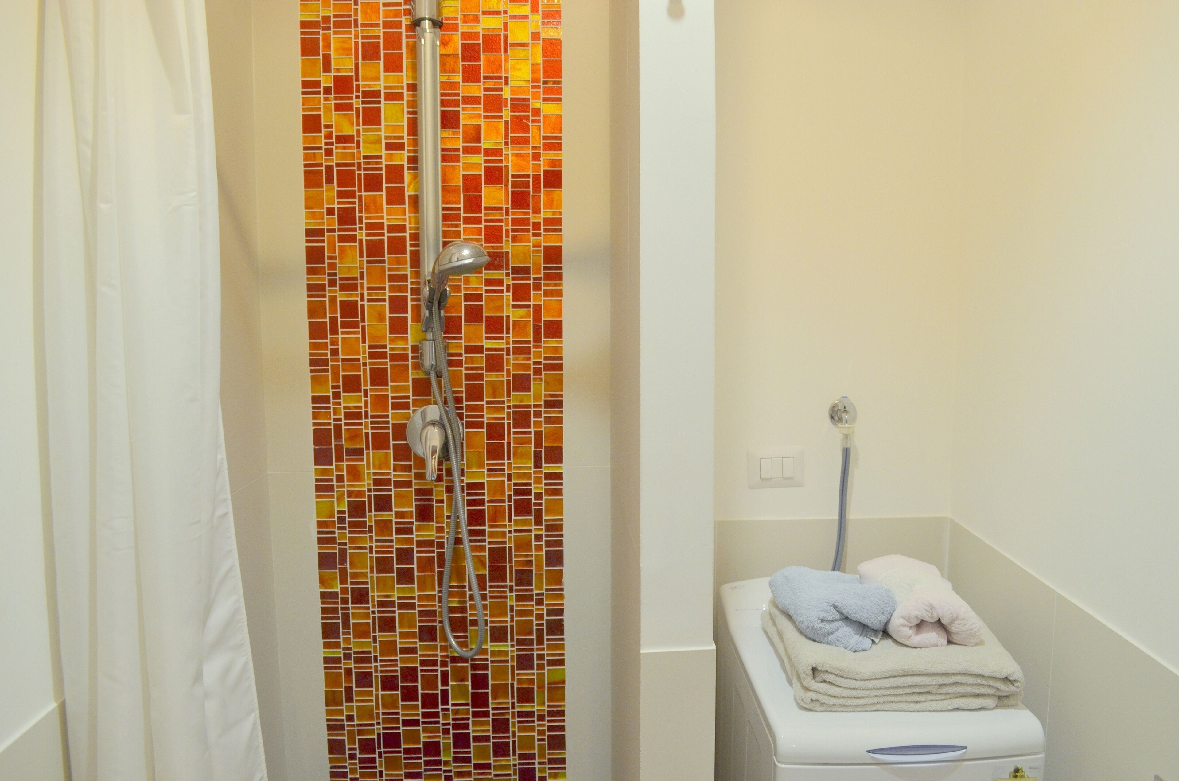 Een badkamer met een douchegedeelte, een betegelde muur met mozaïek, een wit toilet en een handdoekrek met handdoeken.