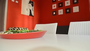Ein Essbereich mit roter Wand, weißem Tisch und einer pinkfarbenen Salatschüssel.