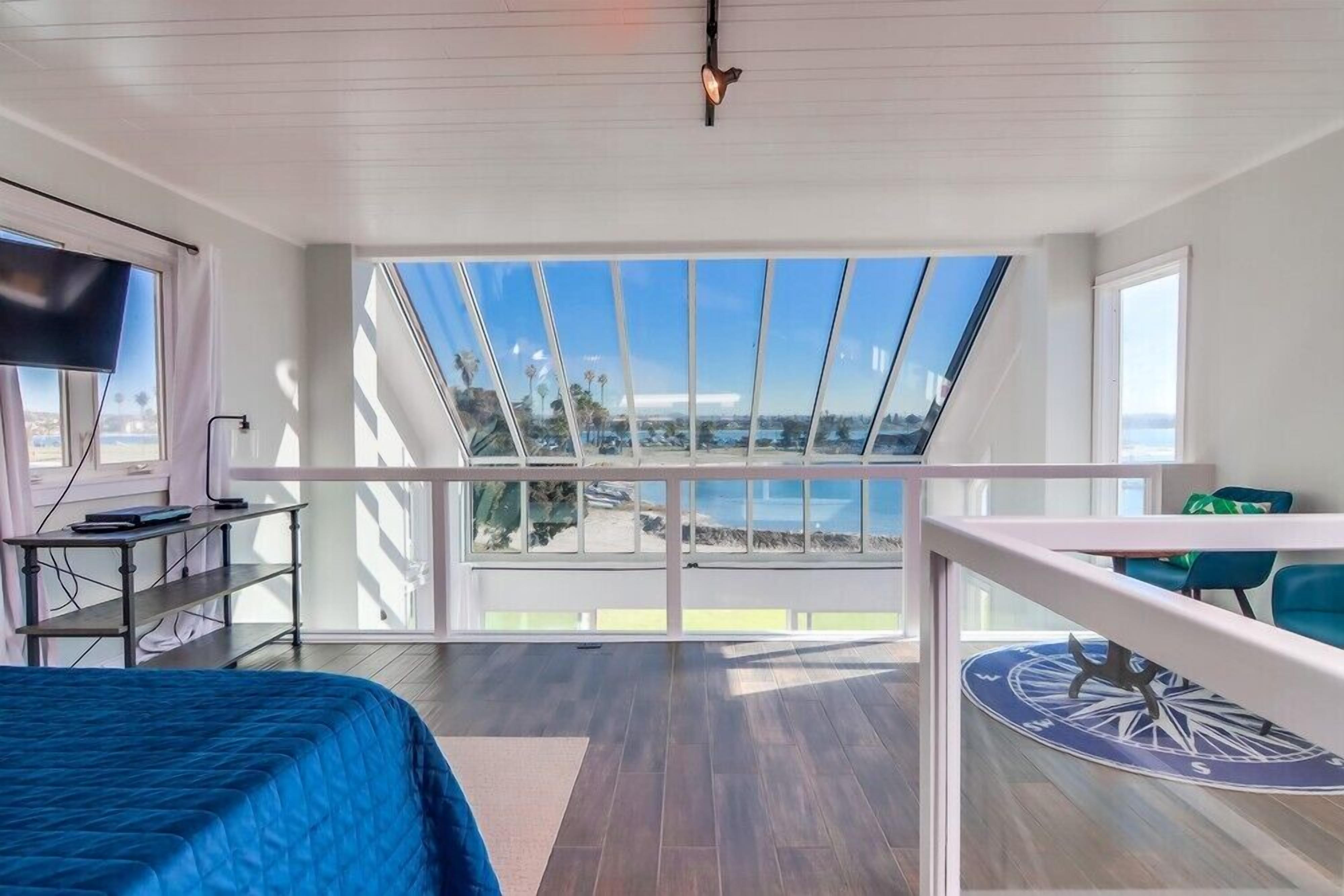 Un dormitorio con una ventana grande, una cama, un escritorio y un televisor.