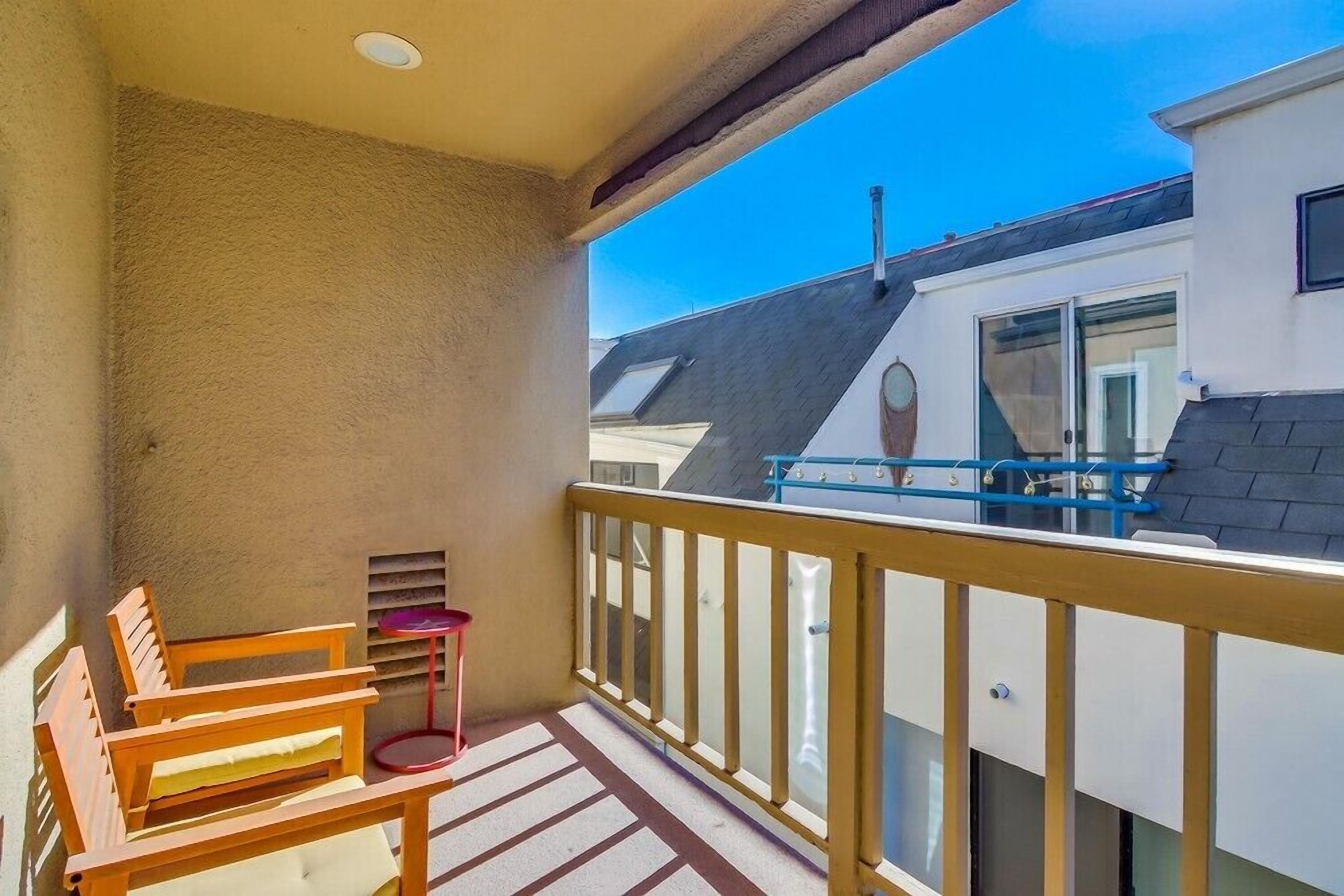 Ein Balkon mit Holzstühlen, einem kleinen Tisch, einem Geländer und Blick auf benachbarte Gebäude.