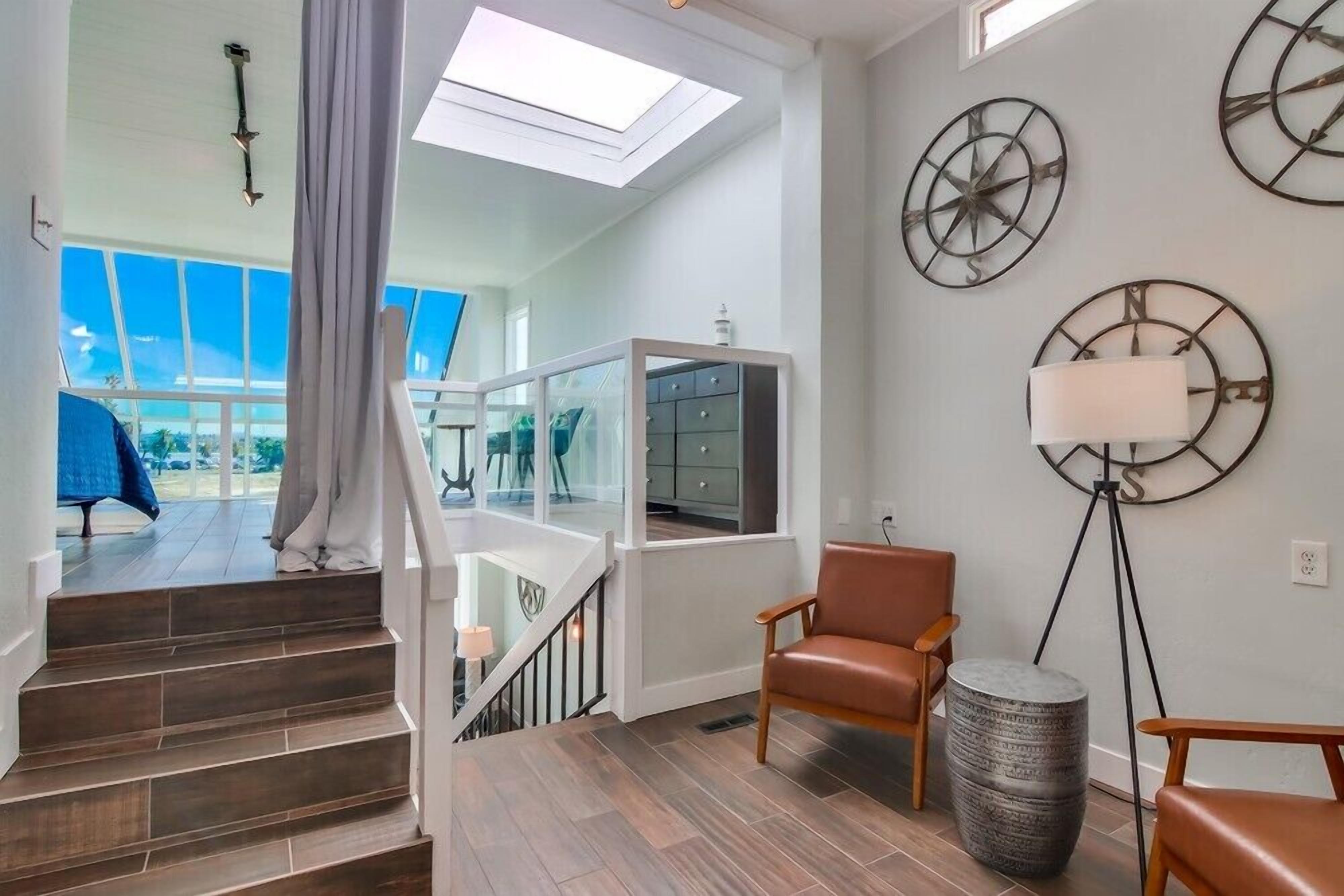 Un interior moderno con una escalera que lleva a un balcón, un sillón de cuero, una lámpara de pie y decoración en la pared.