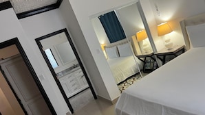 Hotelkamer met een bed, een bureau, een stoel, een spiegel en een badkamer met een wastafel en kastjes.