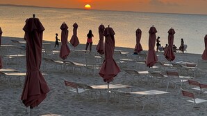 Een strand met rijen ligbedden en parasols, een zonsondergang op de achtergrond en de oceaan.
