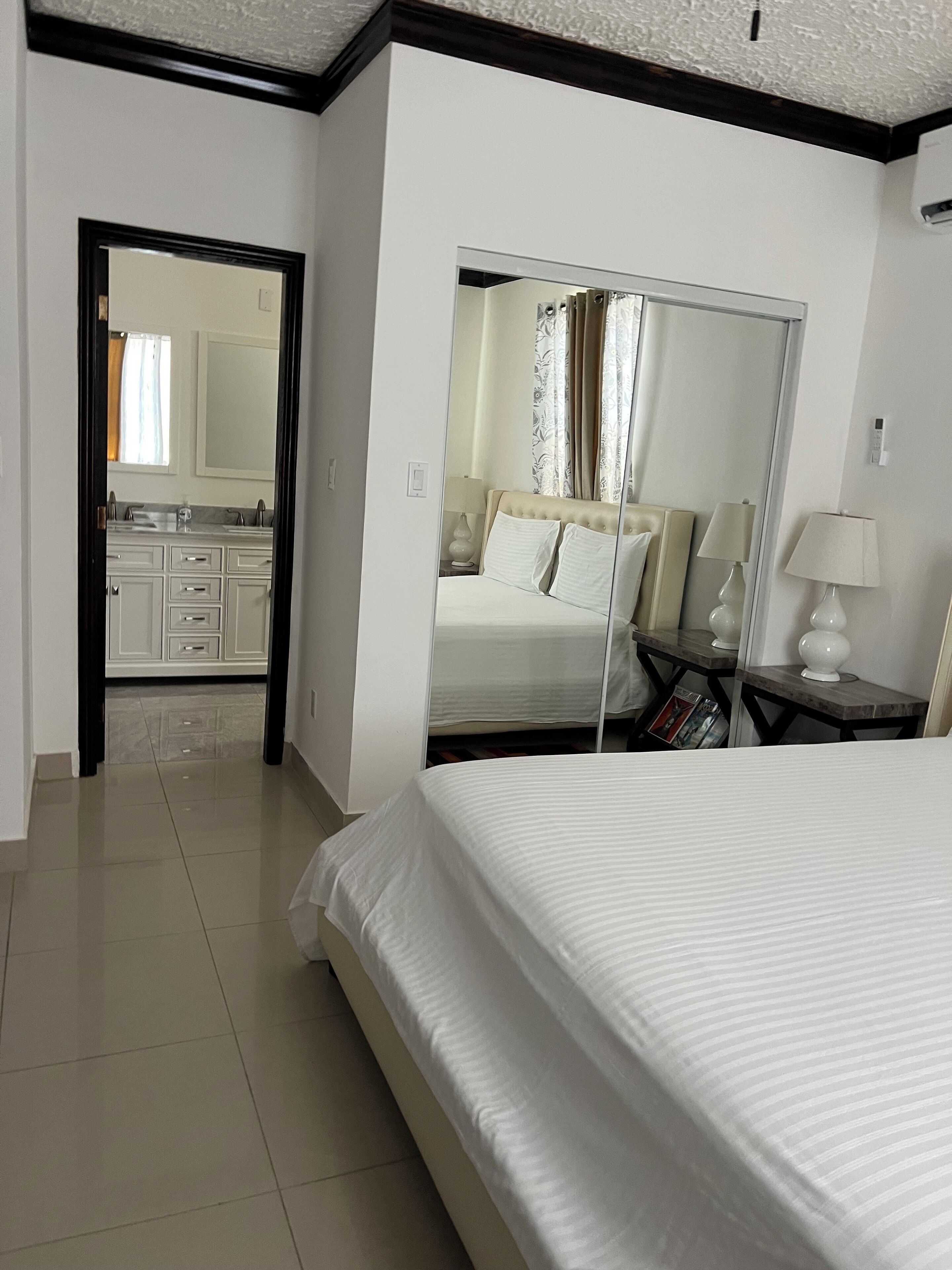 A hotel room with a large bed, a mirror, a nightstand, and a view into the bathroom.