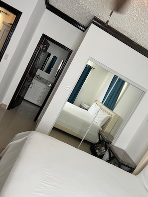 A hotel room with a bed, a bedside table, a mirror, and a door leading to a bathroom. - Island Turquoise Rental (Providenciales)
