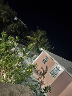A building with a flat roof, a window with a number '45', and surrounding greenery including palm trees and shrubs. - Island Turquoise Rental (Providenciales)