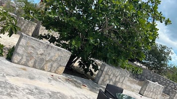 En terrasse med et bord og stole, omgivet af stenvægge og grøn bevoksning.