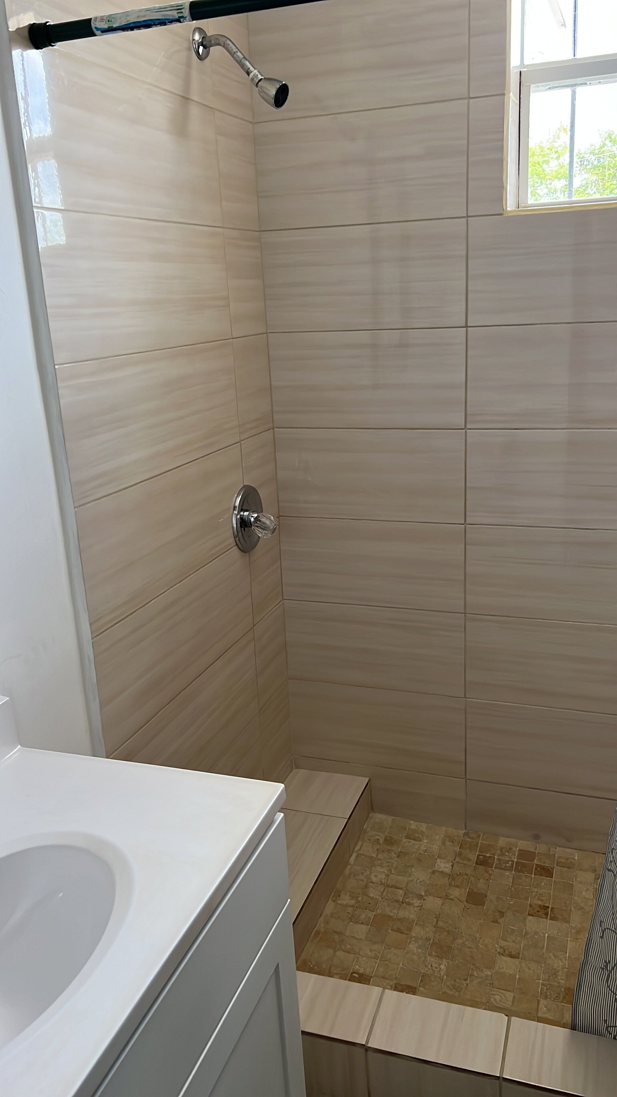 Un área de ducha con puerta de vidrio, un perchero y una ventana.