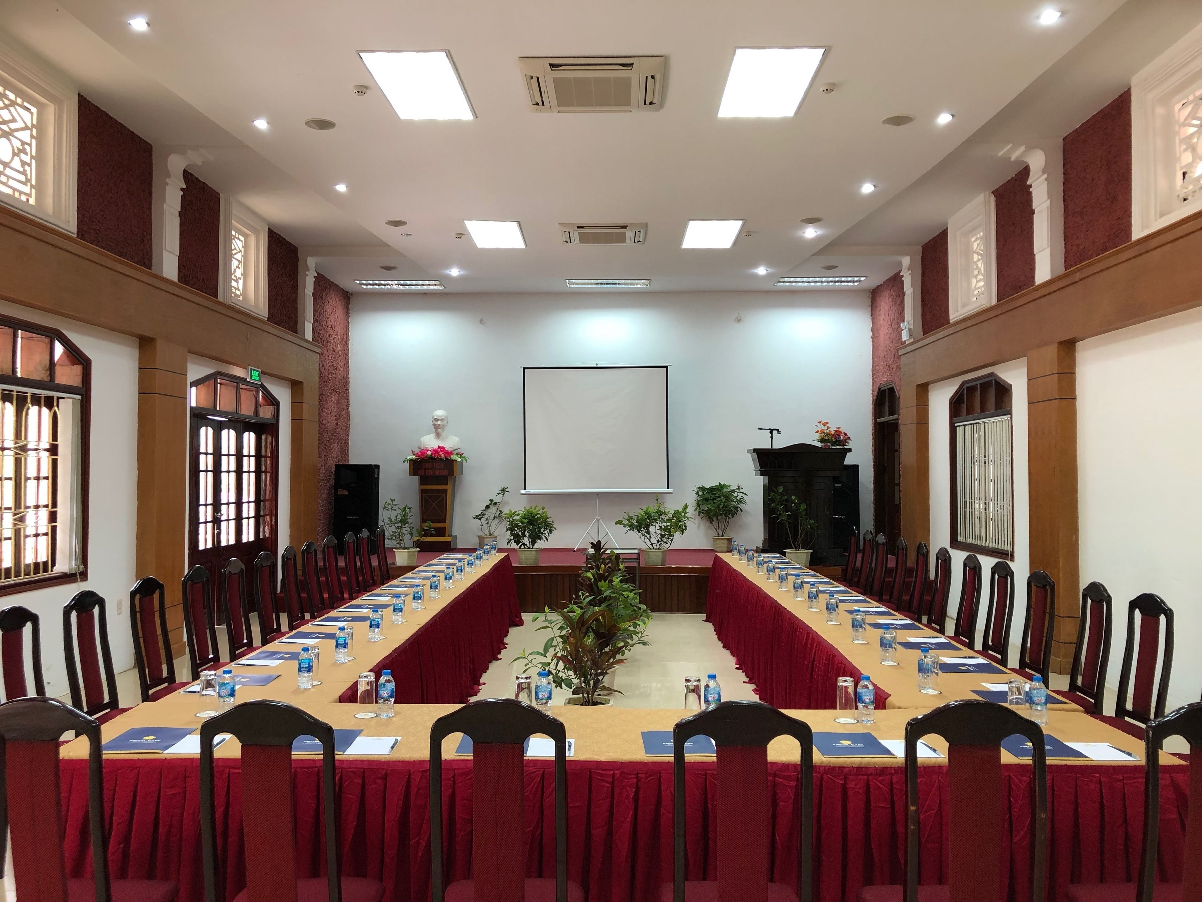 A conference room with a long table, chairs, a podium, and a projector screen.
