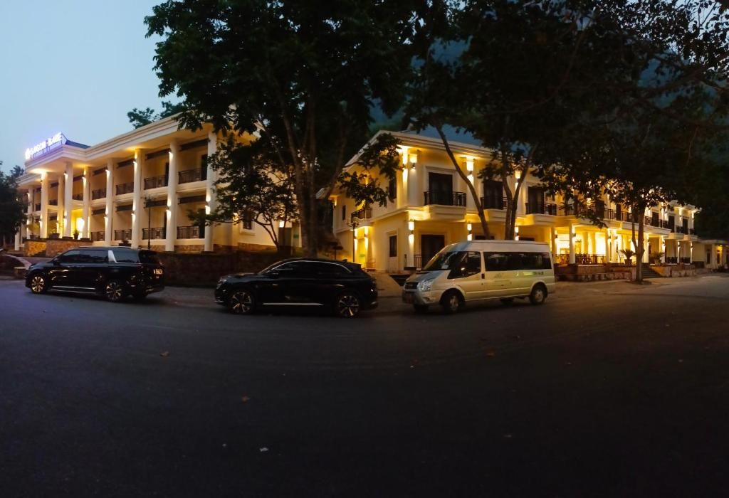 Un hotel de varios pisos con un patio central, coches aparcados y árboles.