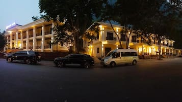 Un hotel de varios pisos con un patio central, coches aparcados y árboles.