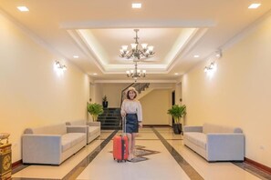 Un vestíbulo de hotel con una escalera central, un candelabro y dos sofás.