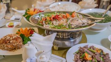 A dining table with various dishes, including a fish dish, a noodle dish, and a beef dish, along with condiments and a teapot.