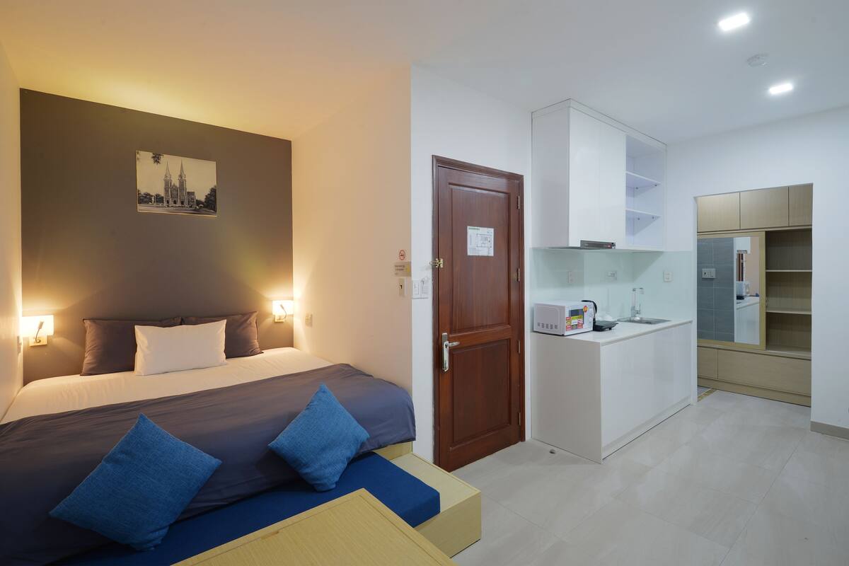 Een kleine hotelkamer met een bed, nachtlampjes, een kitchenette en een deur met een bordje.