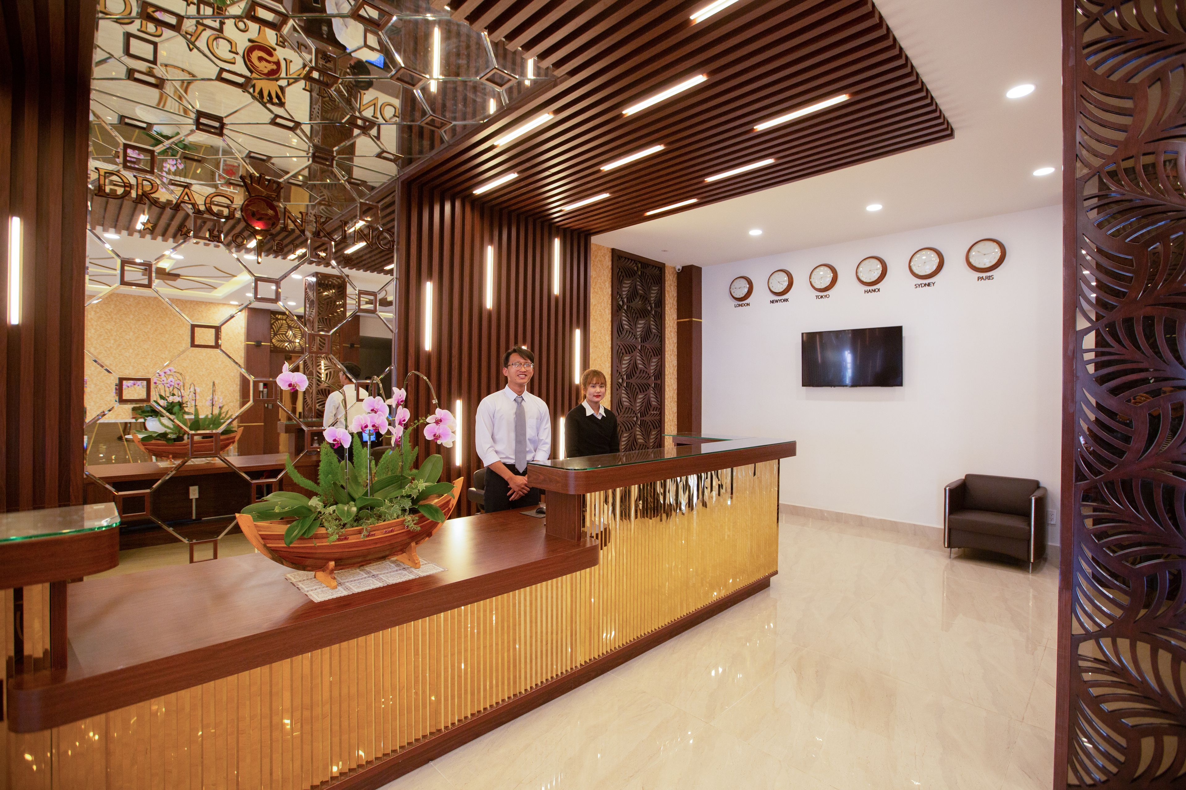 A reception desk with a potted orchid, a wooden panel wall, and a flat-screen TV mounted on the wall.