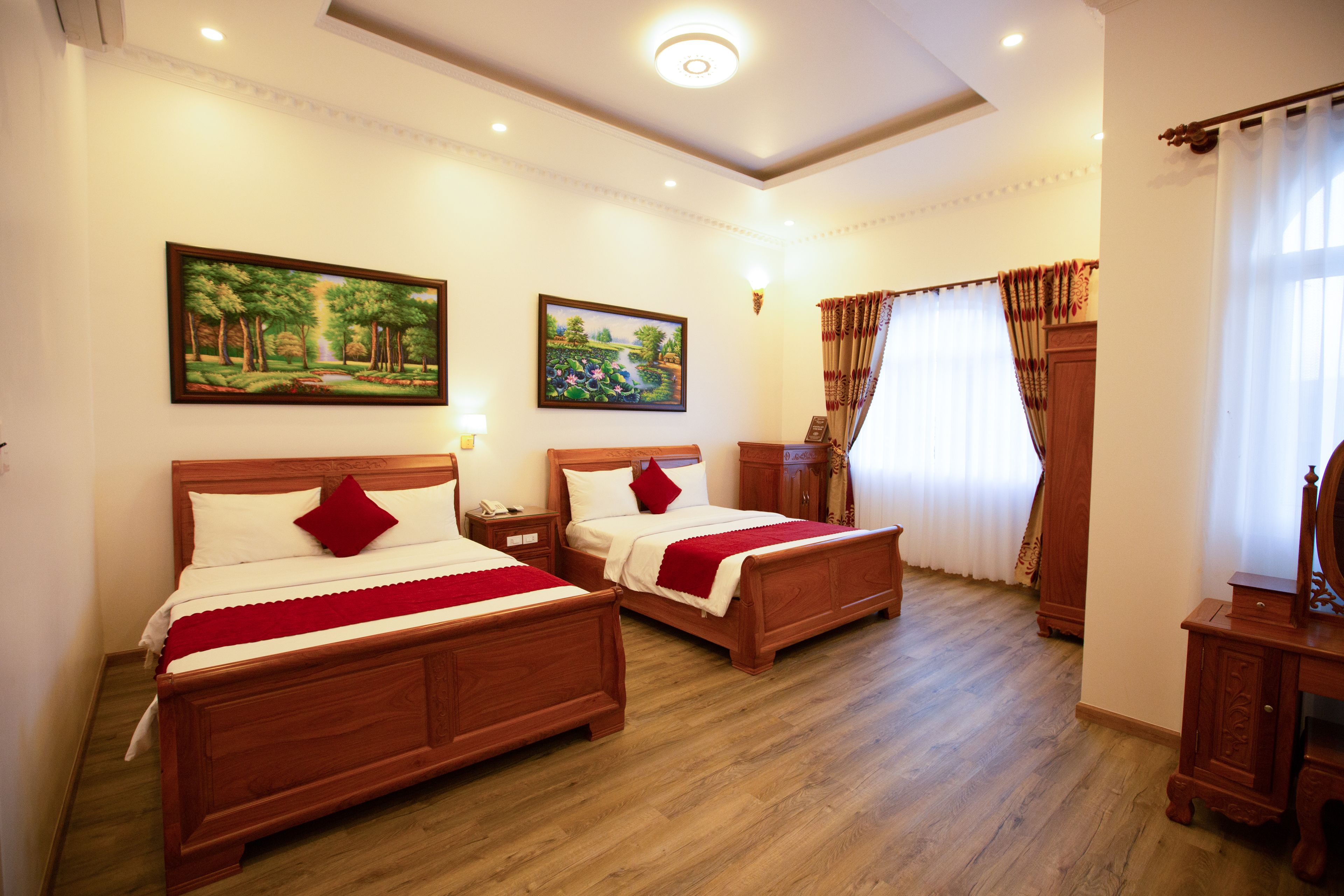 A hotel room with two wooden beds, a nightstand, a dresser, and two paintings on the wall.