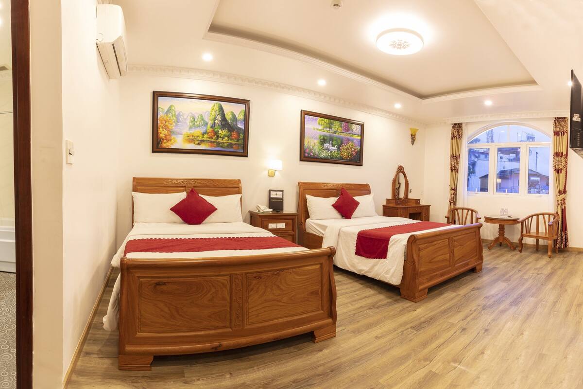 A hotel room with two wooden beds, a bathroom, a small table with chairs, and a window with a view.