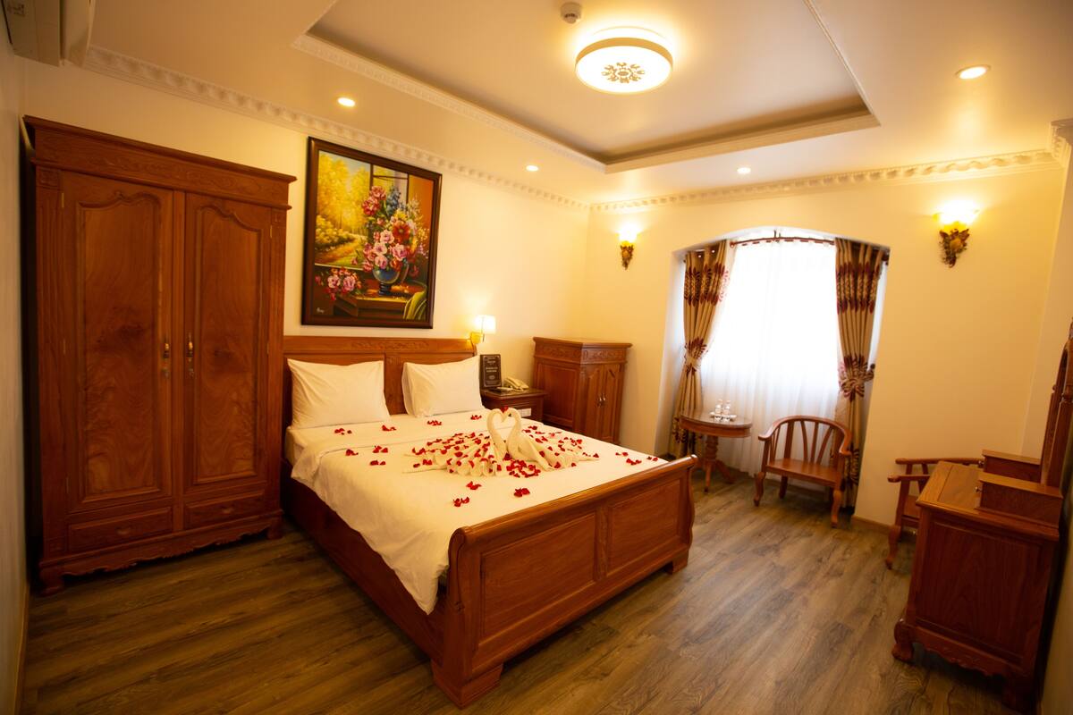 A spacious bedroom with a large wooden bed, a wooden wardrobe, a small wooden table, and a chair.