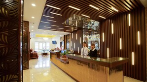 A reception desk with a glass top, wooden paneling, and a modern chandelier. - Dragon King 1 Hotel Da Lat (Xuan Huong - Da Lat)