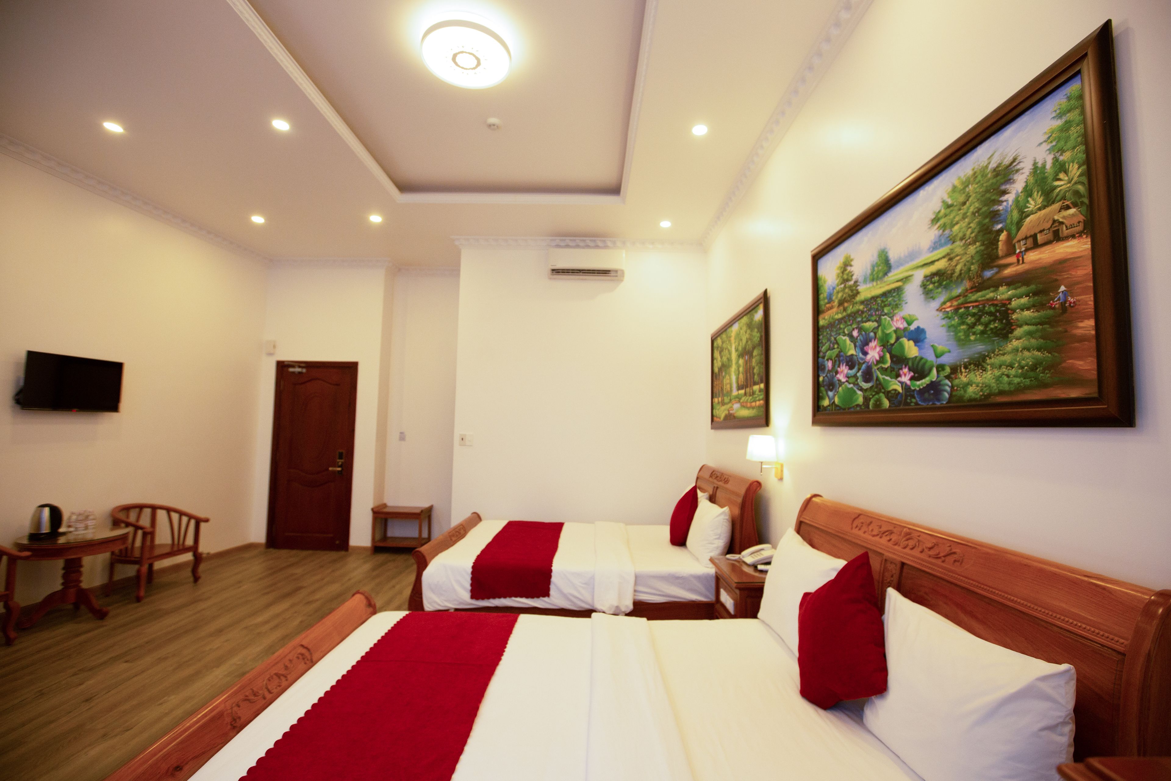 Habitación de hotel con dos camas, piso de madera, un cuadro en la pared, televisor montado y una puerta.
