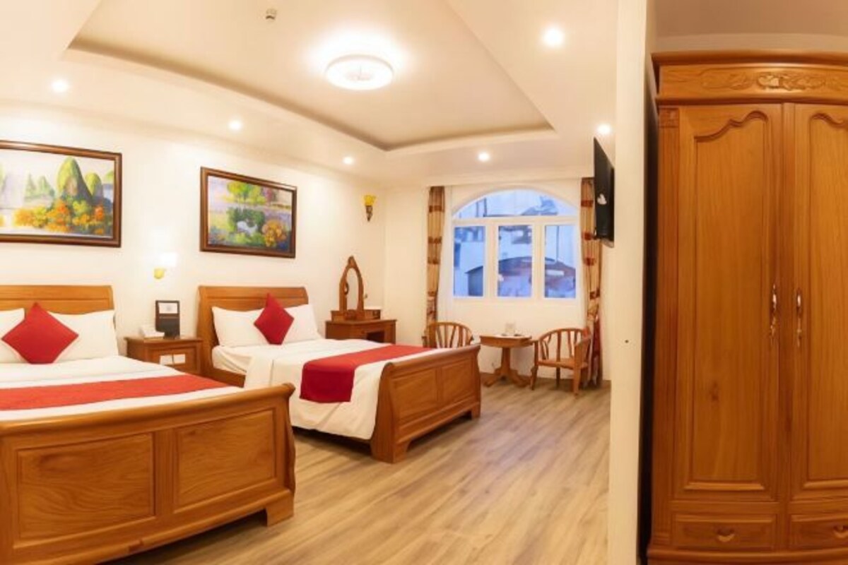 Habitación de hotel con dos camas de madera, un armario de madera, una mesita y una ventana con vistas.