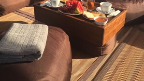 A deck with a wooden table set for breakfast, including bread, fruit, and tea, overlooking a calm lake and green hills. - Perjuangan Boat 2 (Labuan Bajo)