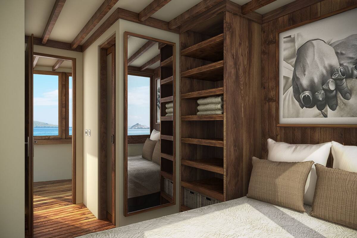 Un dormitorio con un armario grande de madera, una cama con colcha blanca y vistas al mar a través de una ventana.