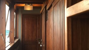 A narrow wooden corridor with a wooden floor, a door with a keyhole, and a window on the left side. - Perjuangan Boat 2 (Labuan Bajo)