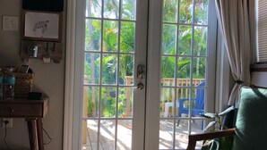 A room with a sliding glass door leading to a patio, a wooden desk with a basket and bottles, a green cushioned chair, and a small rug. - Large lock off room on the backside of our home, 2 miles from beaches. US1&PGA (North Palm Beach)