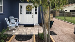 A house with a white door, two lounge chairs, a small garden, and a palm tree. - Large lock off room on the backside of our home, 2 miles from beaches. US1&PGA (North Palm Beach)