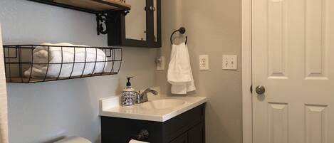 Ein Badezimmer mit Toilette, Waschbecken und Spiegel. Handtücher und eine Seifenspender befinden sich auf dem Waschbecken.