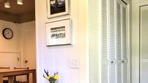 Um corredor com uma mesa de madeira e um vaso de flores, um relógio e uma porta com venezianas.