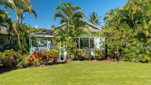 A house with a covered porch, surrounded by lush tropical vegetation and a well-maintained lawn.