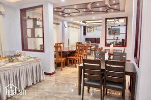 A hotel dining area with multiple tables and chairs, a buffet setup, and a large mirror on the wall. - Hpa An Boutique Inn (Hpa-An)