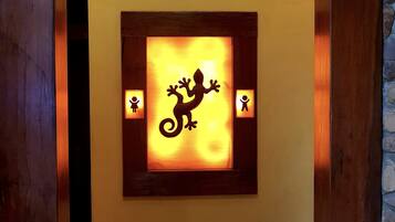 Una pared con una silueta iluminada de lagarto en un marco y dos pequeñas figuras a cada lado.