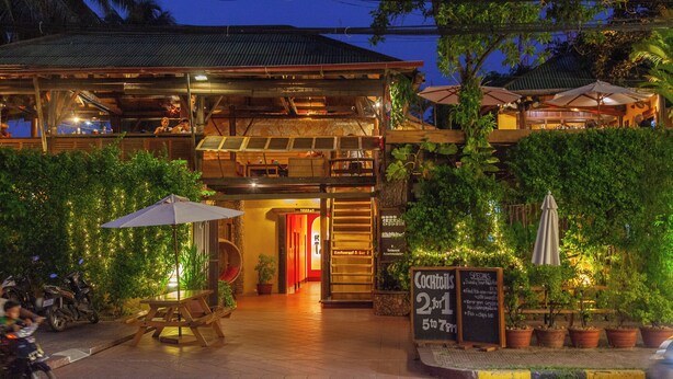 A restaurant with outdoor seating, a covered area, and a sign indicating a cocktail price range. - Rikitikitavi (Kampot)