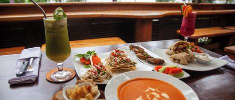 Una mesa con varios platos, incluyendo un tazón de sopa y una fuente de pan, sobre una mesa de madera con bancos al fondo.
