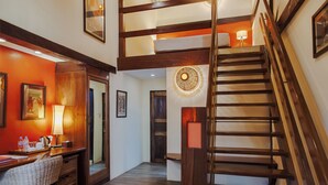 A hotel lobby with a wooden staircase, a desk with a lamp, and framed pictures on the walls. - Rikitikitavi (Kampot)
